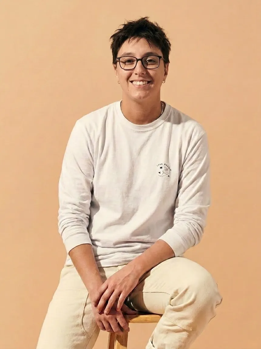 Jamile Ferraz sorrindo, sentada num banquinho de madeira